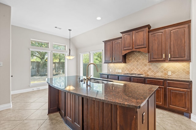 kitchen featuring dark stone countertops, light tile patterned flooring, sink, and an island with sink