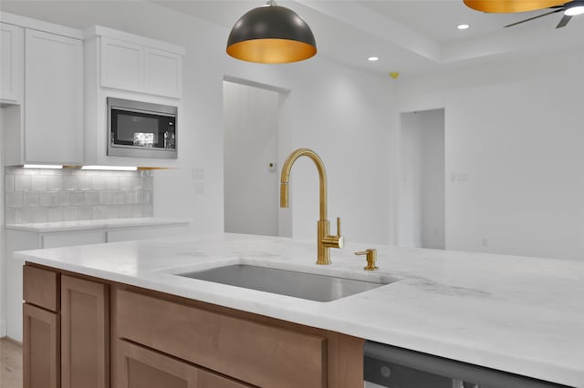 kitchen featuring sink, backsplash, white cabinetry, light stone counters, and built in microwave