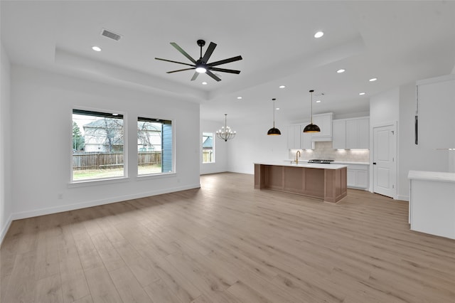 kitchen with light hardwood / wood-style floors, a large island, pendant lighting, white cabinets, and ceiling fan with notable chandelier