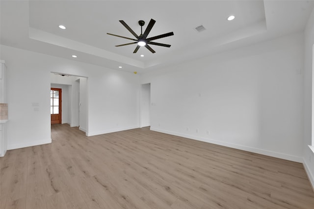 empty room with light hardwood / wood-style flooring, a tray ceiling, and ceiling fan