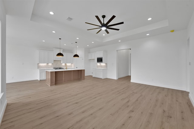 unfurnished living room featuring light hardwood / wood-style flooring, ceiling fan, and a raised ceiling