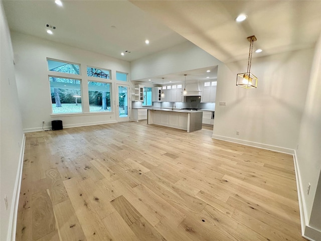 kitchen with light wood-type flooring, tasteful backsplash, a kitchen island, white cabinetry, and hanging light fixtures