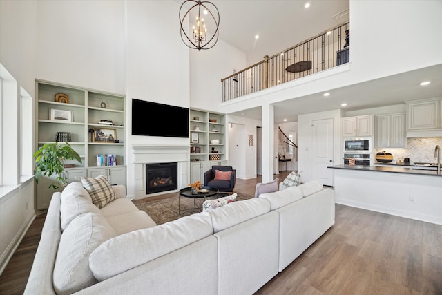 living room with a towering ceiling, a chandelier, sink, and light wood-type flooring