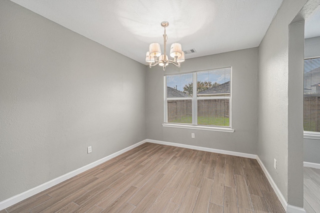 empty room with light hardwood / wood-style flooring and an inviting chandelier