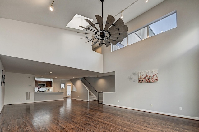 unfurnished living room with a skylight, a towering ceiling, hardwood / wood-style flooring, and ceiling fan