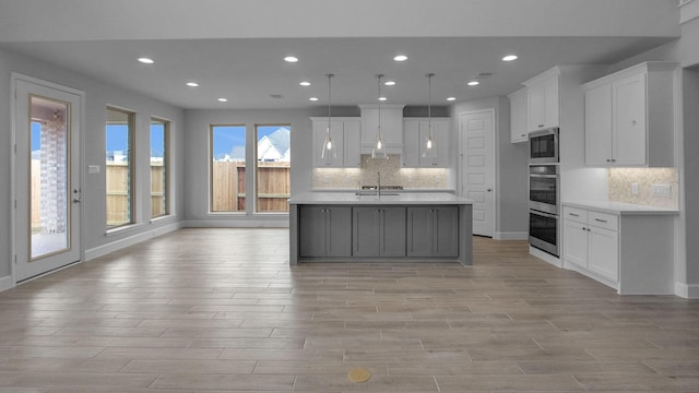 kitchen featuring a center island with sink, white cabinets, hanging light fixtures, light countertops, and a sink