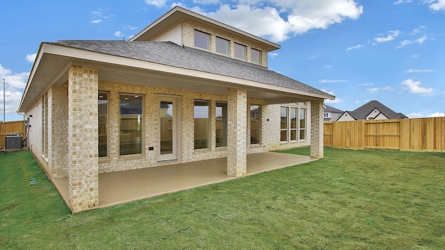 back of property with central AC unit, a patio, roof with shingles, fence, and a yard