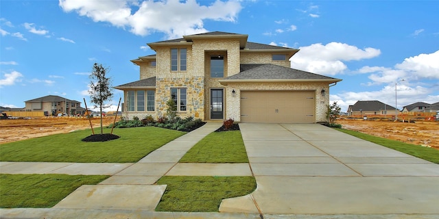 prairie-style house featuring an attached garage, driveway, roof with shingles, and a front yard