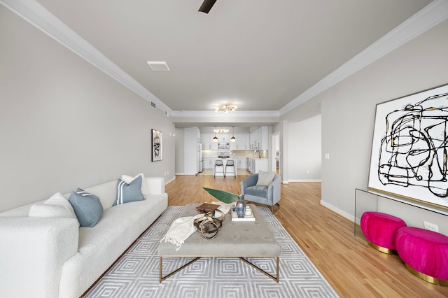 living room with sink, light wood-type flooring, and crown molding