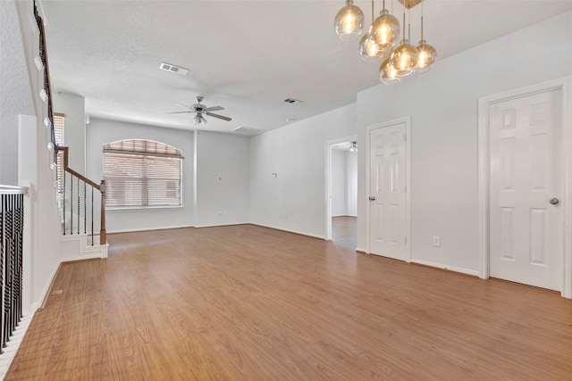 unfurnished living room with light hardwood / wood-style flooring, a textured ceiling, and ceiling fan with notable chandelier