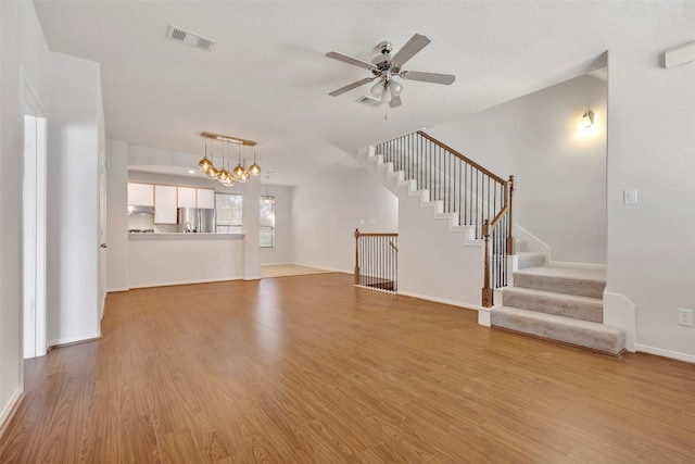 unfurnished living room featuring ceiling fan with notable chandelier and light hardwood / wood-style floors