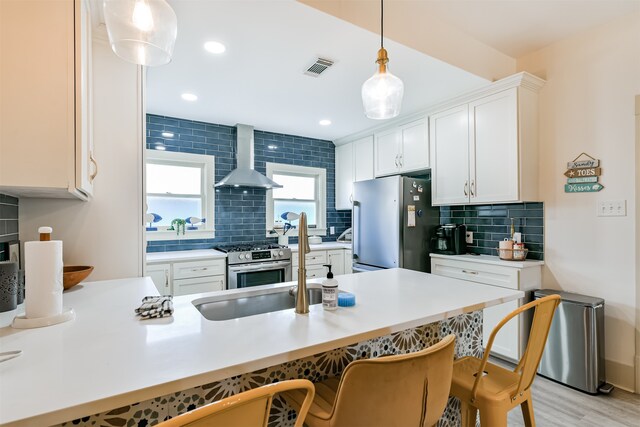 kitchen featuring appliances with stainless steel finishes, light wood-type flooring, wall chimney exhaust hood, white cabinets, and a breakfast bar area