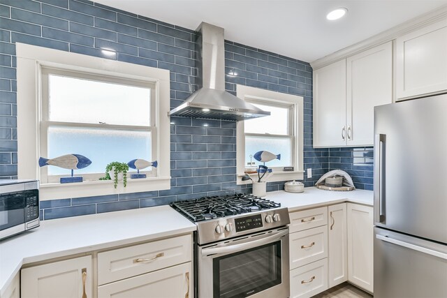 kitchen with stainless steel appliances, wall chimney exhaust hood, decorative backsplash, and white cabinets