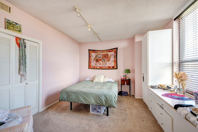 bedroom with track lighting, light carpet, multiple windows, and a closet