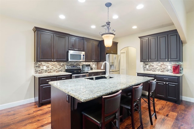 kitchen featuring dark hardwood / wood-style flooring, tasteful backsplash, stainless steel appliances, sink, and an island with sink