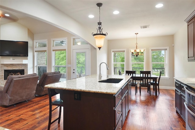 kitchen featuring a center island with sink, sink, dark hardwood / wood-style floors, a fireplace, and dark brown cabinetry