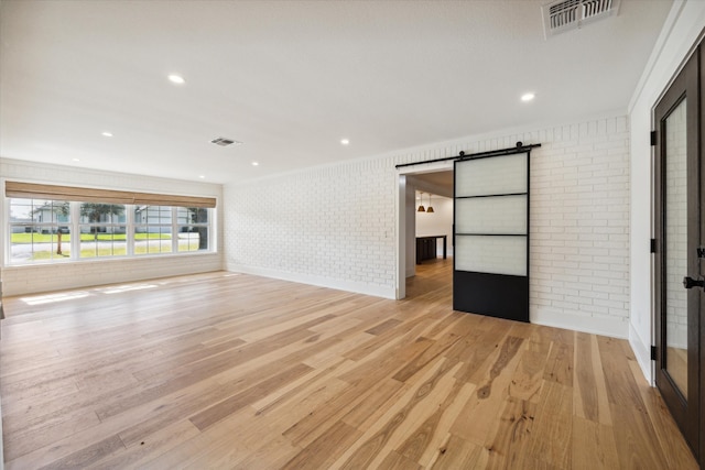 unfurnished living room with brick wall, a barn door, and light hardwood / wood-style flooring