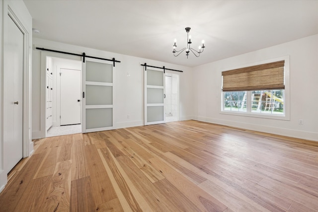 unfurnished bedroom with light hardwood / wood-style floors, a notable chandelier, and a barn door