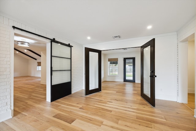 unfurnished bedroom featuring light hardwood / wood-style flooring, french doors, a barn door, and brick wall