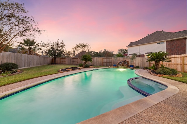 pool at dusk with an in ground hot tub and a yard