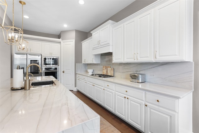 kitchen with light stone countertops, appliances with stainless steel finishes, decorative light fixtures, white cabinets, and dark hardwood / wood-style floors