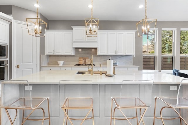 kitchen with a kitchen bar, decorative light fixtures, light stone counters, and a large island with sink