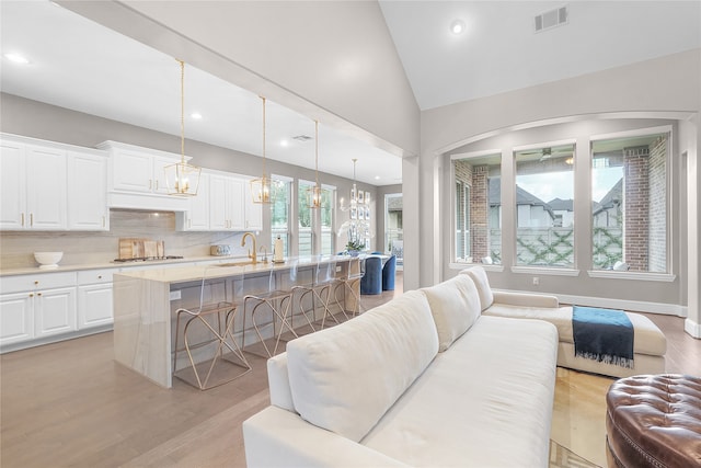 living room with sink, vaulted ceiling, light hardwood / wood-style flooring, and an inviting chandelier