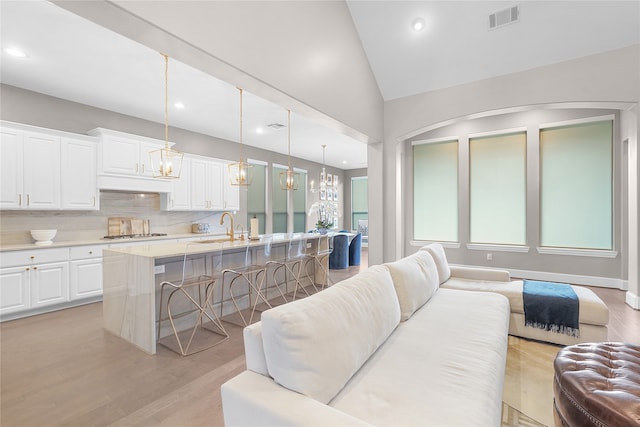 living room featuring sink, light hardwood / wood-style flooring, vaulted ceiling, and a chandelier