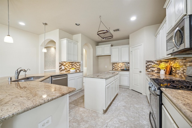 kitchen featuring hanging light fixtures, a kitchen island, decorative backsplash, white cabinets, and appliances with stainless steel finishes