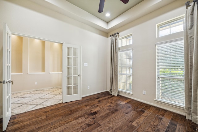 empty room with a tray ceiling, dark hardwood / wood-style flooring, ceiling fan, and french doors