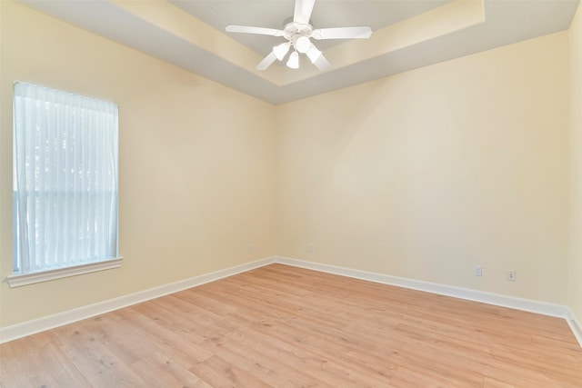 spare room with ceiling fan, a tray ceiling, and light hardwood / wood-style flooring