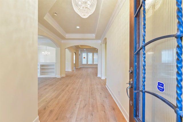 hallway with light hardwood / wood-style floors, a raised ceiling, crown molding, and a chandelier