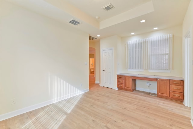 interior space with a raised ceiling, built in desk, and light hardwood / wood-style flooring