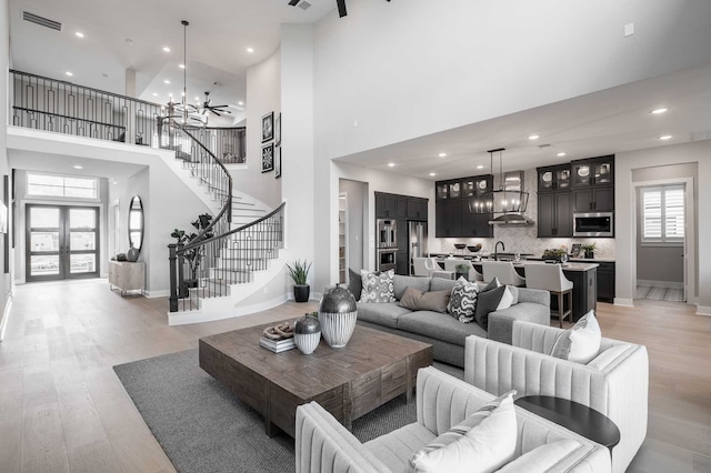 living room featuring sink, a towering ceiling, an inviting chandelier, and light wood-type flooring