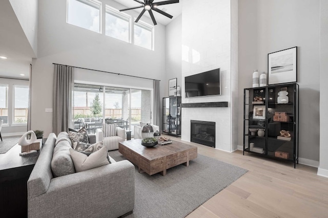 living room featuring a towering ceiling, light hardwood / wood-style flooring, plenty of natural light, and a tile fireplace