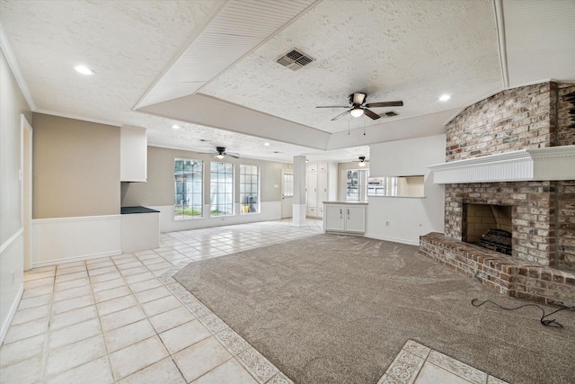 unfurnished living room featuring ceiling fan, a brick fireplace, crown molding, a textured ceiling, and light carpet