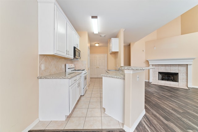 kitchen featuring white cabinets, light wood-type flooring, gas range gas stove, a tile fireplace, and light stone counters