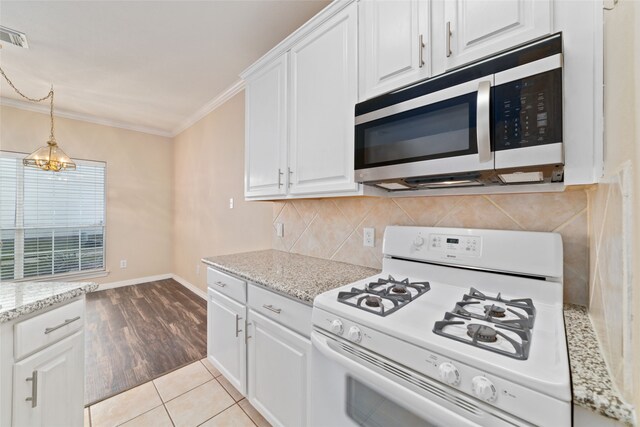 kitchen with gas range gas stove, white cabinets, light stone counters, ornamental molding, and light hardwood / wood-style flooring