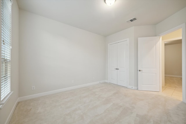 unfurnished bedroom with multiple windows, light carpet, and a closet