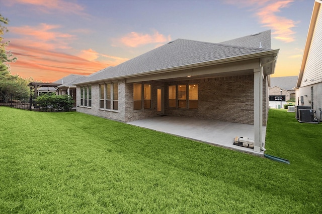 back house at dusk with a yard, a patio area, and central air condition unit