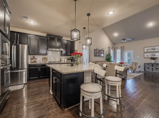 kitchen with an island with sink, backsplash, dark hardwood / wood-style flooring, stainless steel appliances, and decorative light fixtures