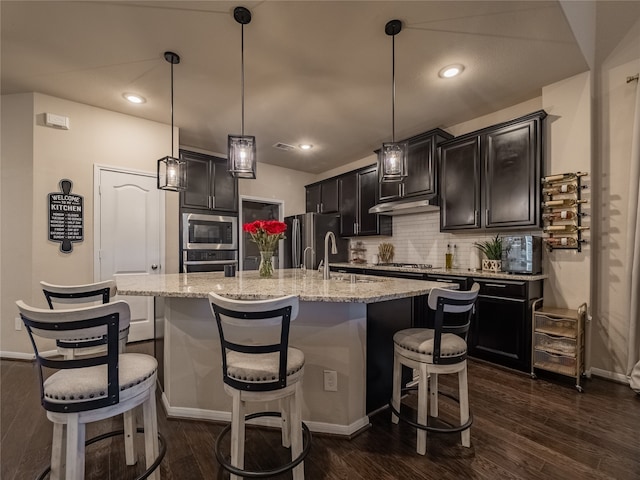 kitchen featuring an island with sink, appliances with stainless steel finishes, dark hardwood / wood-style flooring, a kitchen bar, and pendant lighting