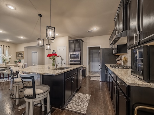 kitchen featuring dark wood-type flooring, an island with sink, range hood, sink, and decorative light fixtures