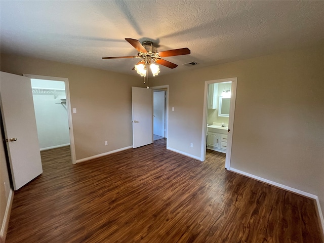 unfurnished bedroom with dark wood-type flooring, a walk in closet, ceiling fan, connected bathroom, and a closet