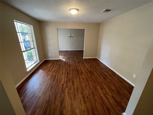 unfurnished room featuring a textured ceiling, a chandelier, and dark hardwood / wood-style floors