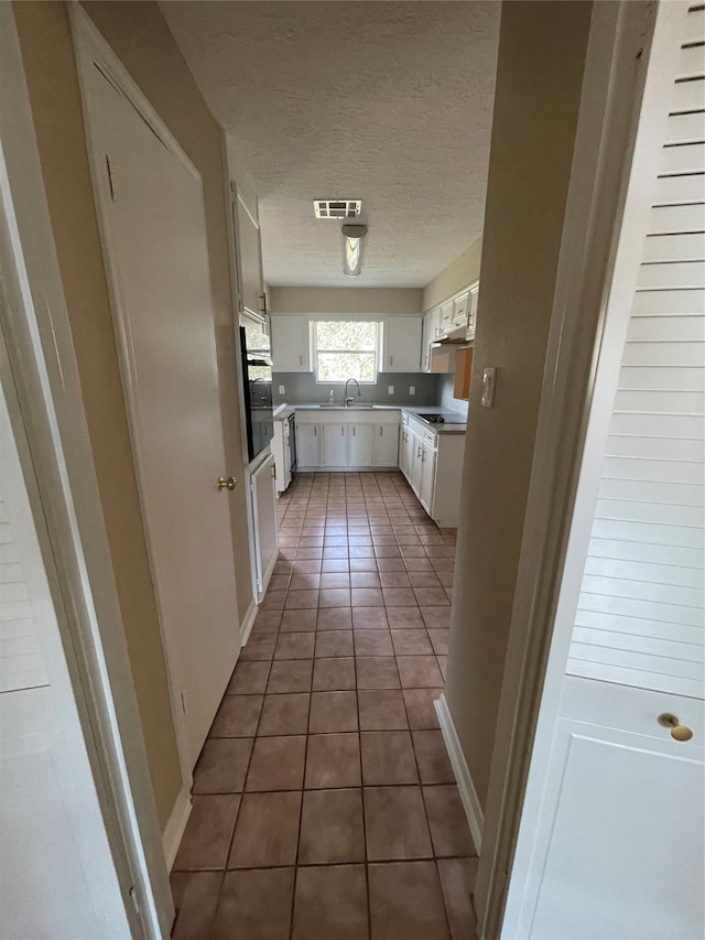 kitchen featuring white cabinets, oven, dark tile patterned flooring, sink, and a textured ceiling