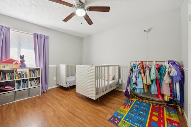 bedroom featuring hardwood / wood-style floors, a nursery area, a textured ceiling, and ceiling fan