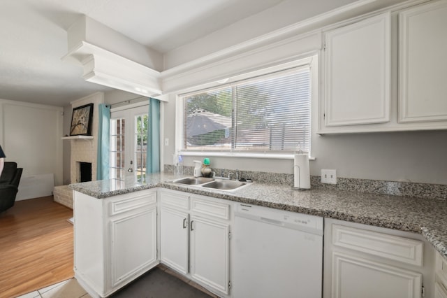 kitchen with dishwasher, wood-type flooring, sink, a brick fireplace, and white cabinetry