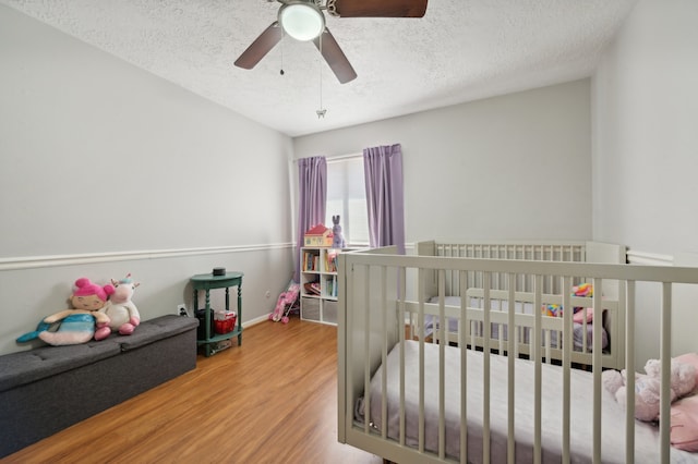 bedroom with hardwood / wood-style floors, a textured ceiling, a crib, and ceiling fan