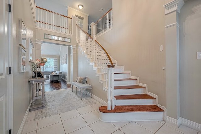 stairway featuring a high ceiling, decorative columns, and tile patterned flooring